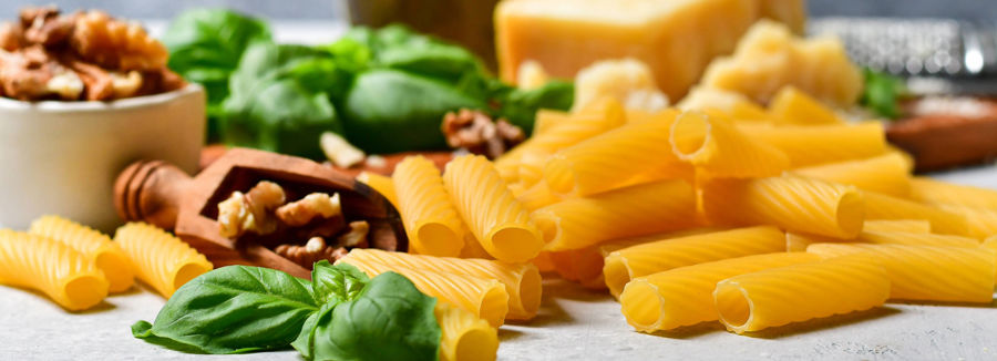 Ingredients on a marble kitchen worksurface including dry pasta, fresh basil and walnuts